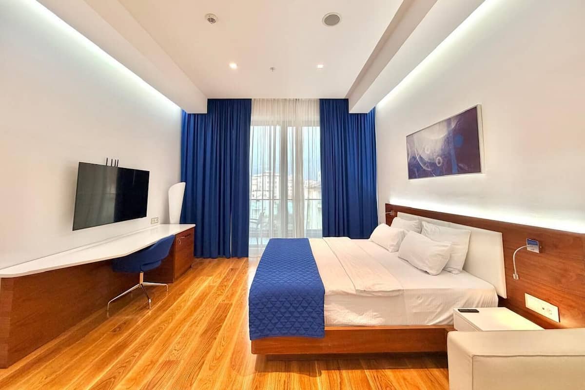 A hotel room with a bed, a desk, a TV, and a large window with curtains.