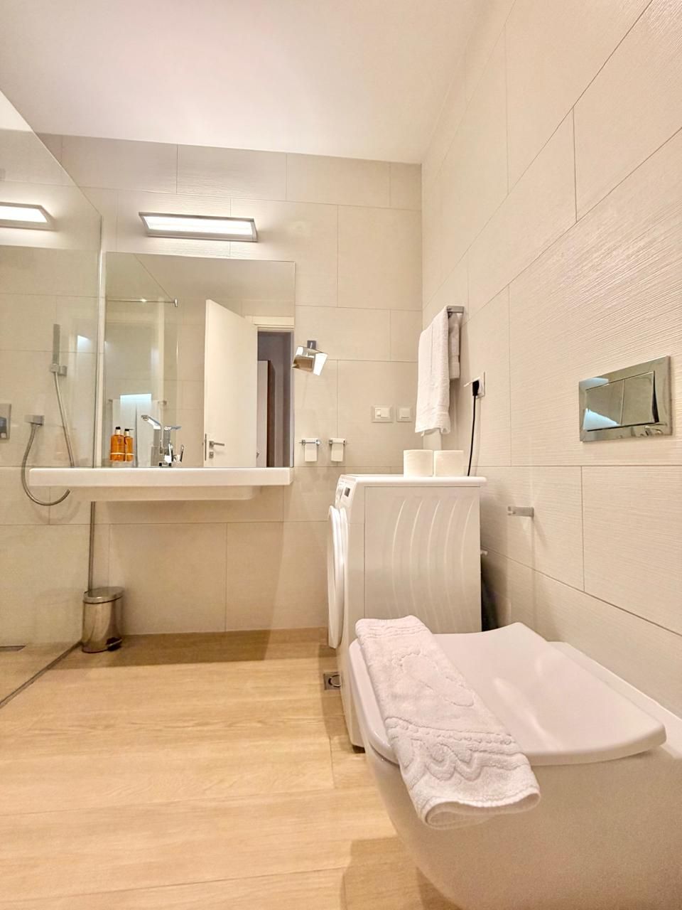 Un baño moderno con ducha de vidrio, lavamanos blanco y una toalla en el suelo.