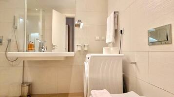 Un baño moderno con ducha de vidrio, lavamanos blanco y una toalla en el suelo.