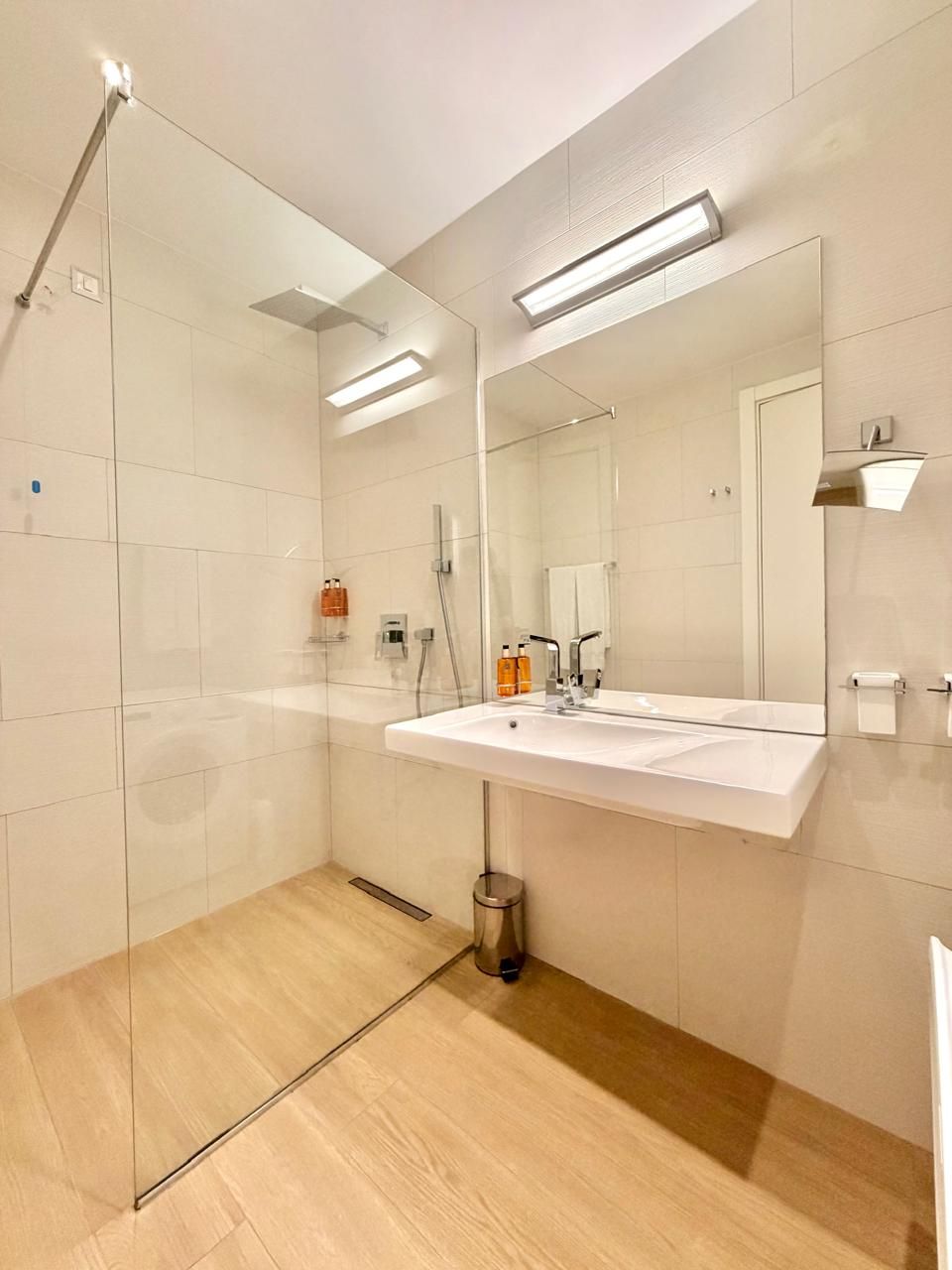 Un baño moderno con cabina de ducha de vidrio, un lavabo blanco y un espejo grande.