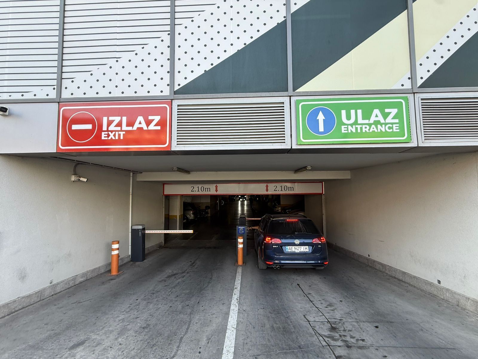 Entrada a un estacionamiento con un coche, letreros de SALIDA y ENTRADA, y marcas de altura.