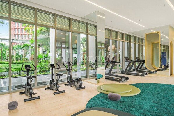 A modern gym with cardio machines, a mirror, and a view of greenery outside. - Taveli by Kozystay - TB Simatupang (Jakarta)