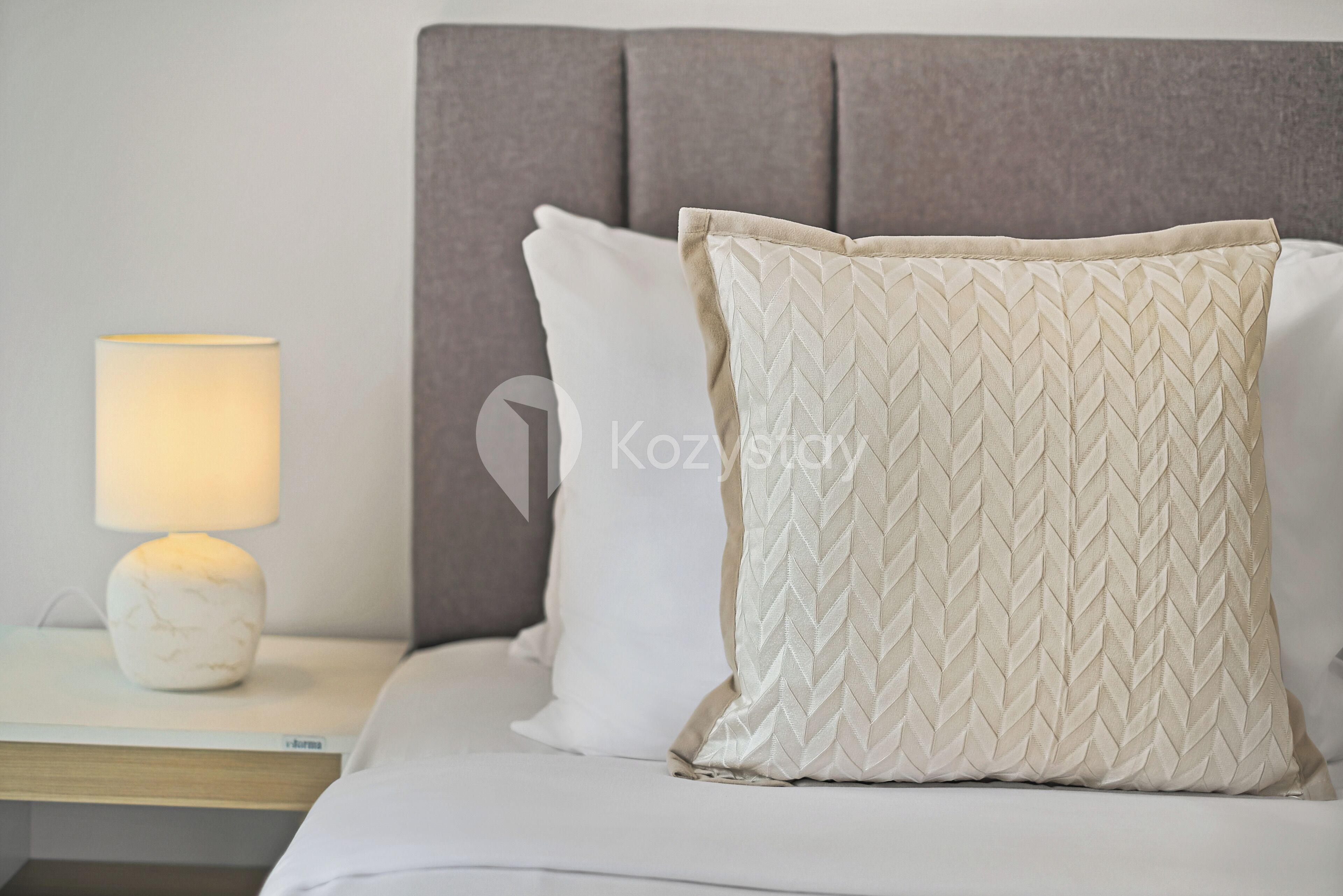 Una cama bien hecha con cabecera, lámpara de noche y almohada con textura.
