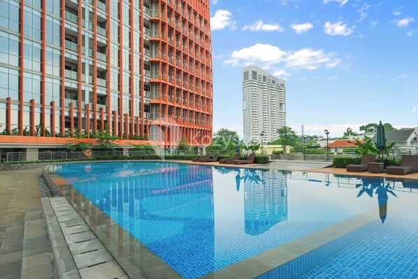 A swimming pool with a tiled deck, surrounded by modern buildings with balconies and a clear sky. - Taveli by Kozystay - TB Simatupang (Jakarta)