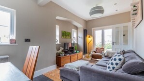 A modern living room with a sofa, a TV, a lamp, and a dining area. - Beautiful 5 bedroom House in smart suburb. Close to beautiful Lake & Parkland. (Cardiff)