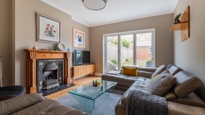 A living room with a fireplace, sofa, and glass coffee table. - Beautiful 5 bedroom House in smart suburb. Close to beautiful Lake & Parkland. (Cardiff)