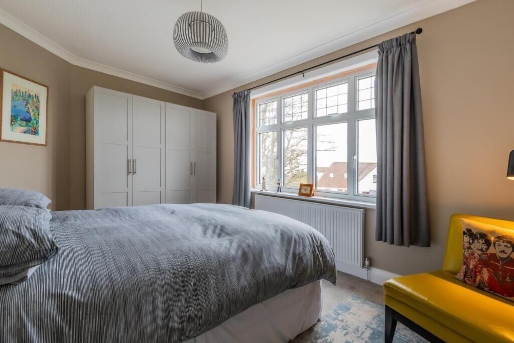 Un dormitorio con cama, armario, ventana con cortinas y una silla amarilla.