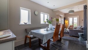 A dining area with a table, chairs, and a vase of flowers. There are windows and a clock on the wall. - Beautiful 5 bedroom House in smart suburb. Close to beautiful Lake & Parkland. (Cardiff)