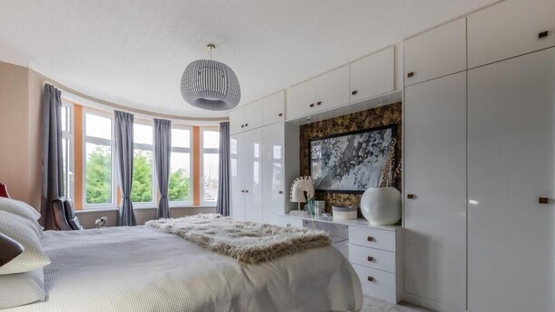 A bedroom with a large bed, a wardrobe, a painting, and a window with curtains. - Beautiful 5 bedroom House in smart suburb. Close to beautiful Lake & Parkland. (Cardiff)