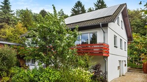 Ein modernes, zweistöckiges Haus mit geneigtem Dach, einem Balkon und einem Garten.