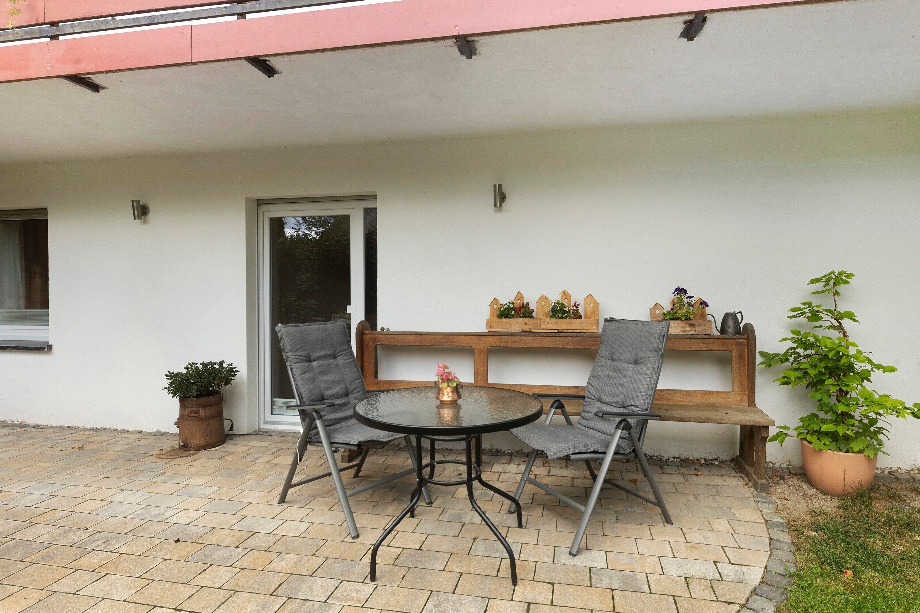 An outdoor patio with a round table and two chairs, a wooden bench, and potted plants.