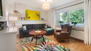 Ein modernes Wohnzimmer mit einer Couch, einem Sessel, einem Couchtisch und einem großen Fenster mit Blick auf Grünflächen.