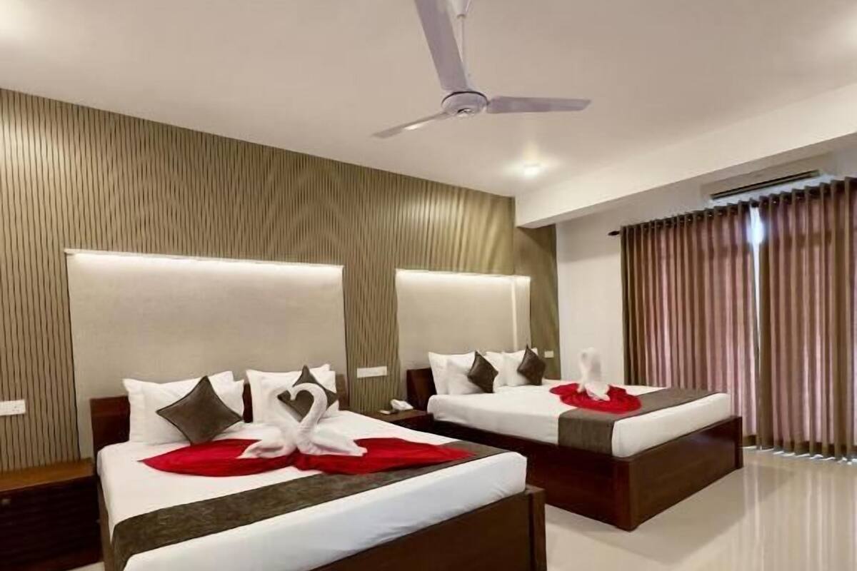 A modern hotel room with two beds, a ceiling fan, and a large window with curtains.
