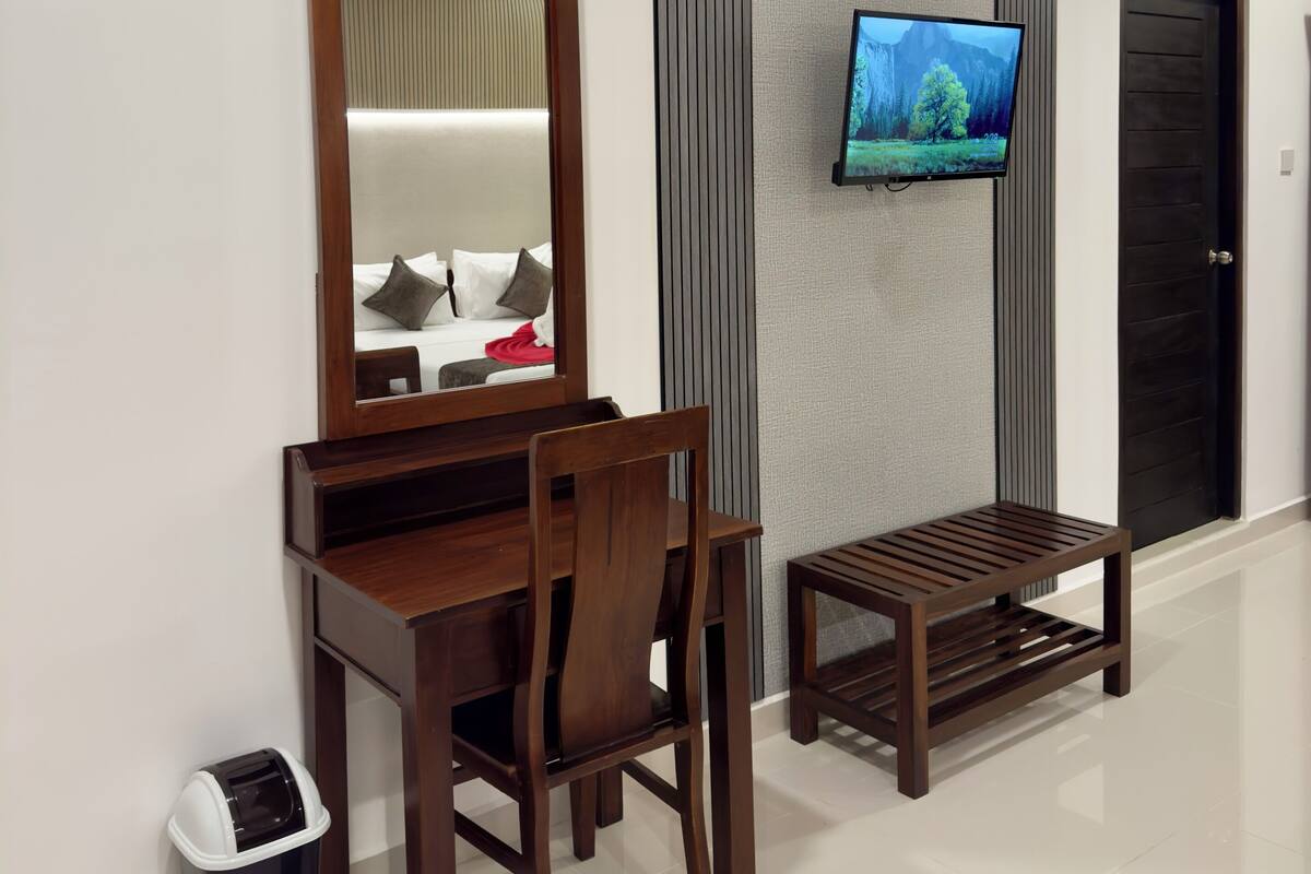 A modern hotel room with a wooden desk, a chair, a television mounted on the wall, and a door in the background.
