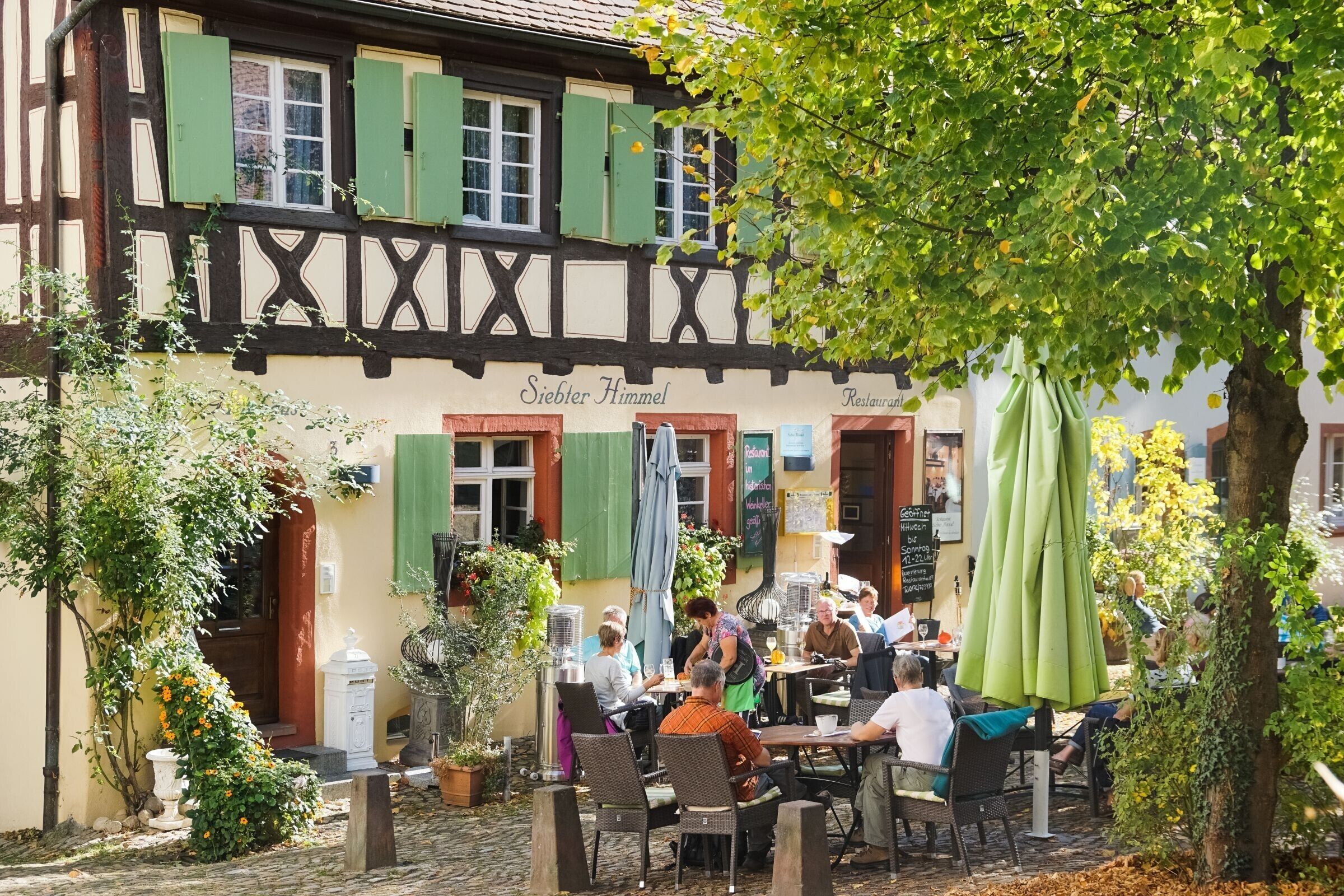 A traditional half-timbered building with outdoor seating and a sign reading 'Siebter Himmel Restaurant.'