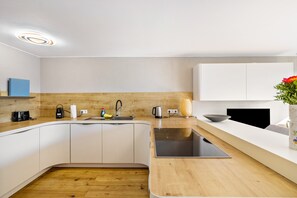 Une cuisine moderne avec des armoires blanches, un comptoir en bois, un évier encastré et un petit îlot central doté d’une cuisinière.