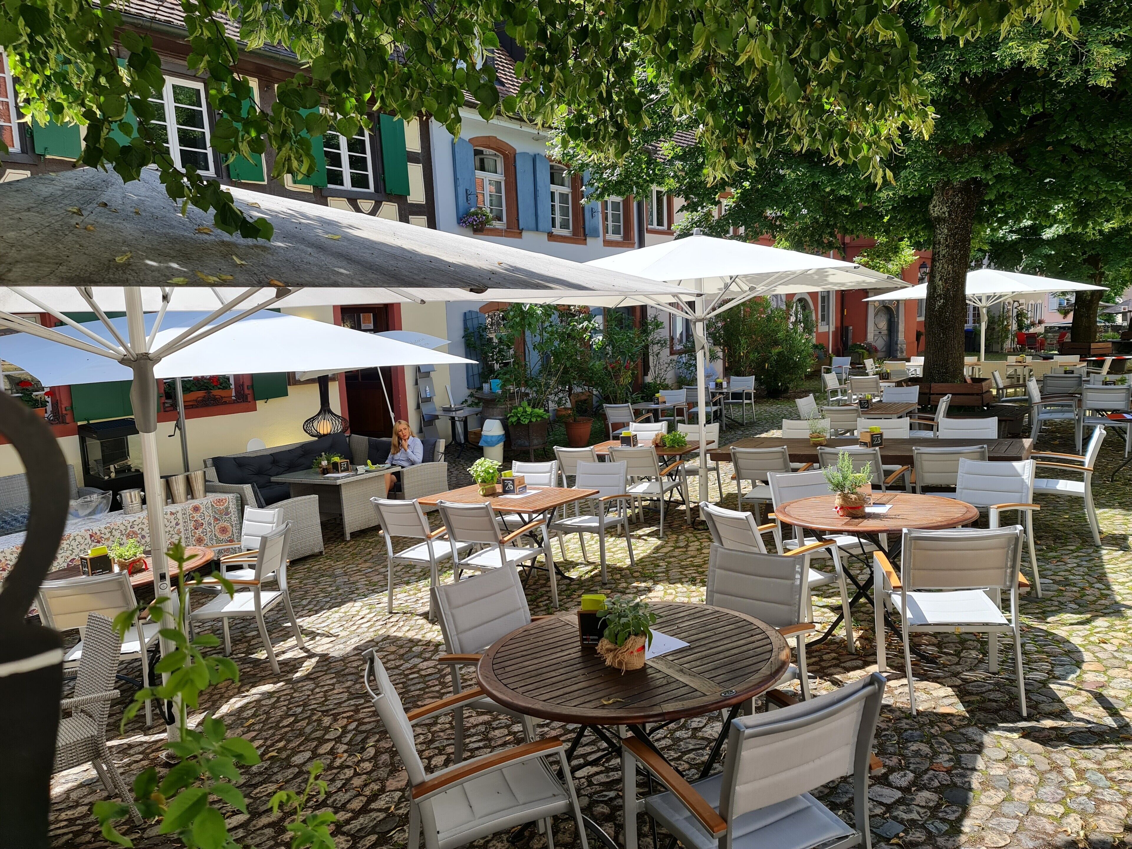 An outdoor café with tables and chairs, surrounded by buildings and trees.
