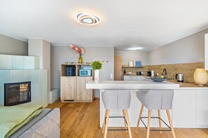 A modern kitchen with a white countertop, two grey bar stools, a microwave, and a wooden cabinet.