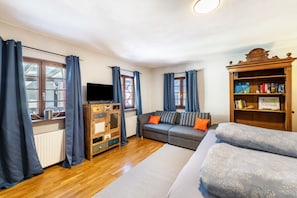 A room with a wooden cabinet, a sofa, a television, and a bookshelf. - Merlot Apartment Standard 40m² with Balcony for 2 Guests, Optional Breakfast, 3D Tour Website (Vogtsburg)