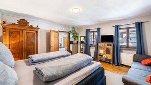 A room with a bed, a sofa, a wooden cabinet, a television, and a window with curtains.