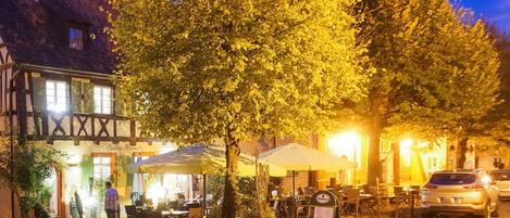 Una calle adoquinada con mesas al aire libre, un árbol y un edificio con un letrero que dice 'Siebmacher Hammel'.