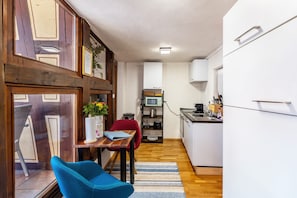 A compact kitchen with a microwave, stove, and sink. A dining area with a table and chairs is visible, and a small refrigerator is in the corner. - Merlot Apartment Standard 40m² with Balcony for 2 Guests, Optional Breakfast, 3D Tour Website (Vogtsburg)