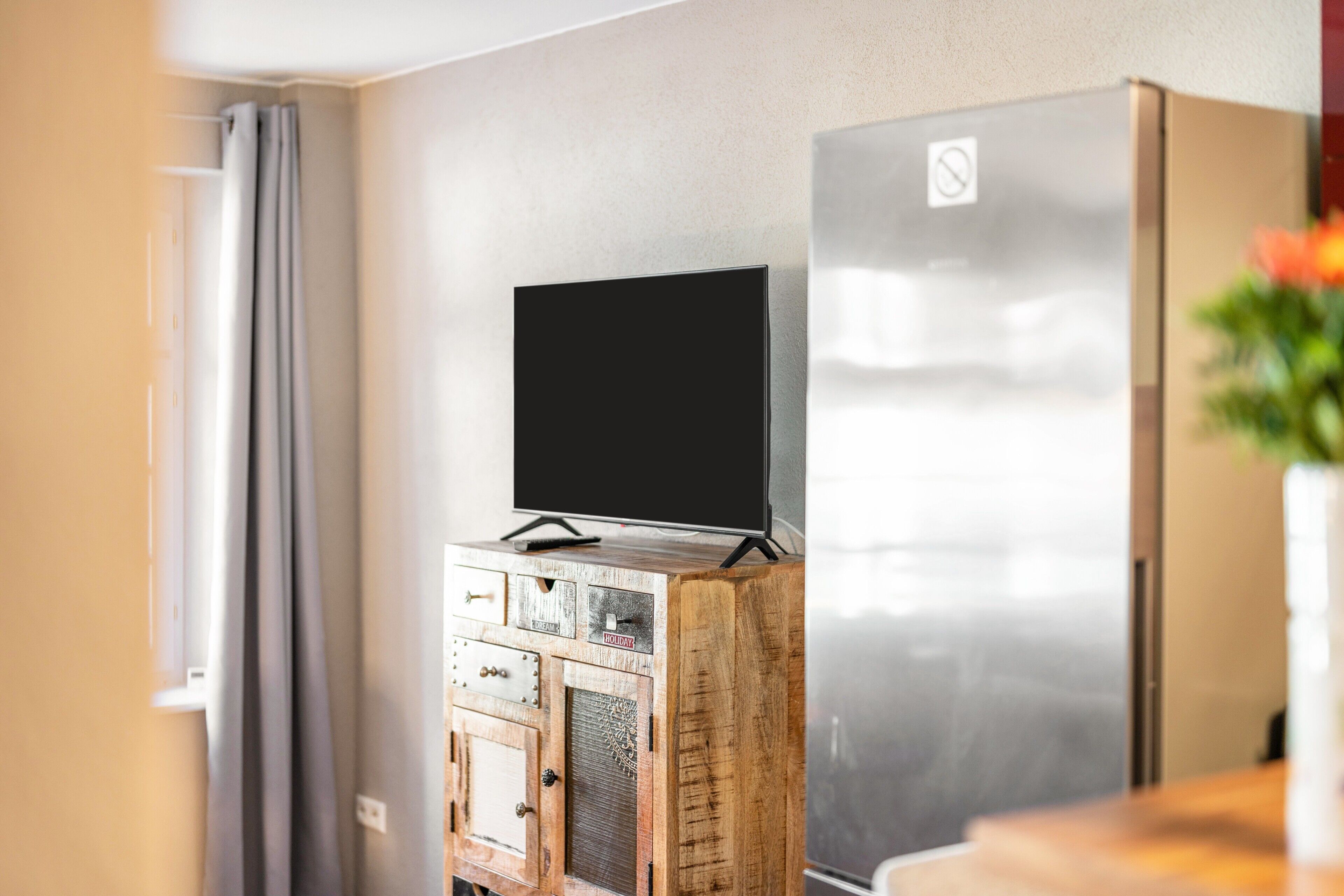 A room with a wooden cabinet, a television on top, and a stainless steel refrigerator.
