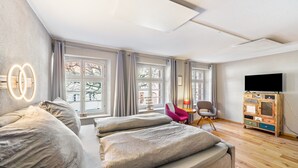 Une chambre d’hôtel moderne avec un grand lit, une télévision, une armoire en bois et de grandes fenêtres.