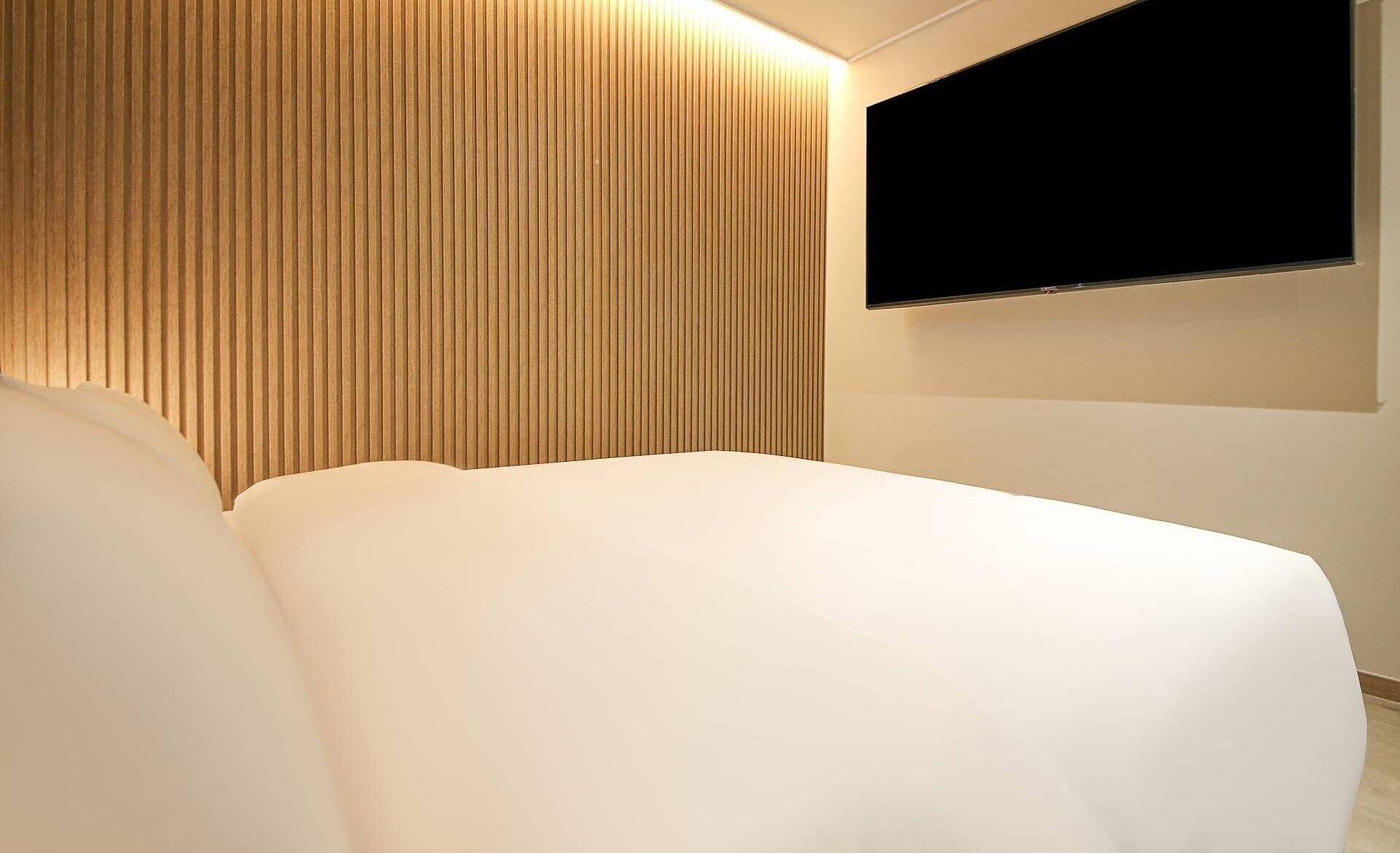 Ett modernt hotellrum med en stor säng, ett huvudgavel av träribbor och en platt-TV som är monterad på väggen.