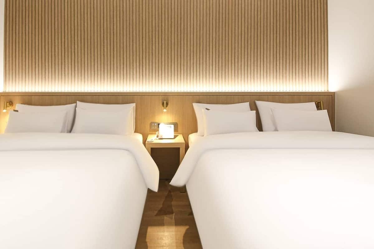 A hotel room with two beds, a nightstand with a lamp, and a wooden headboard.