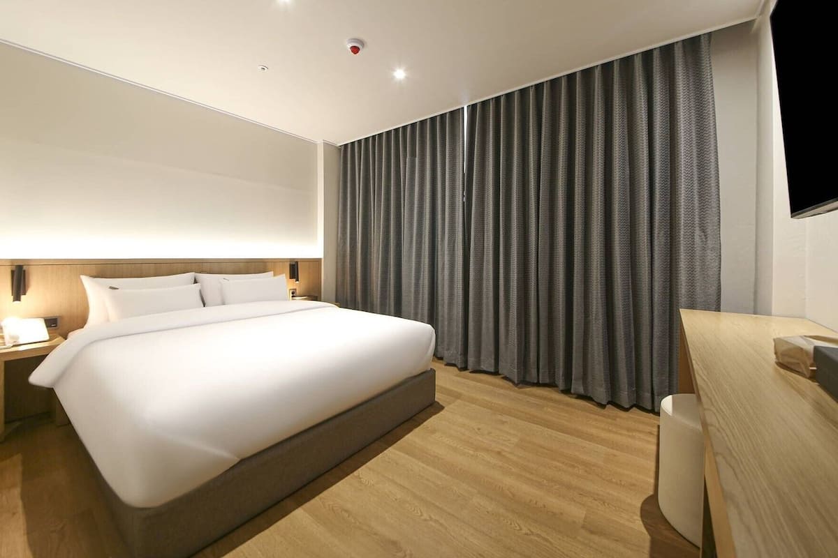 A modern hotel room with a large bed, wooden flooring, a desk, and a TV.