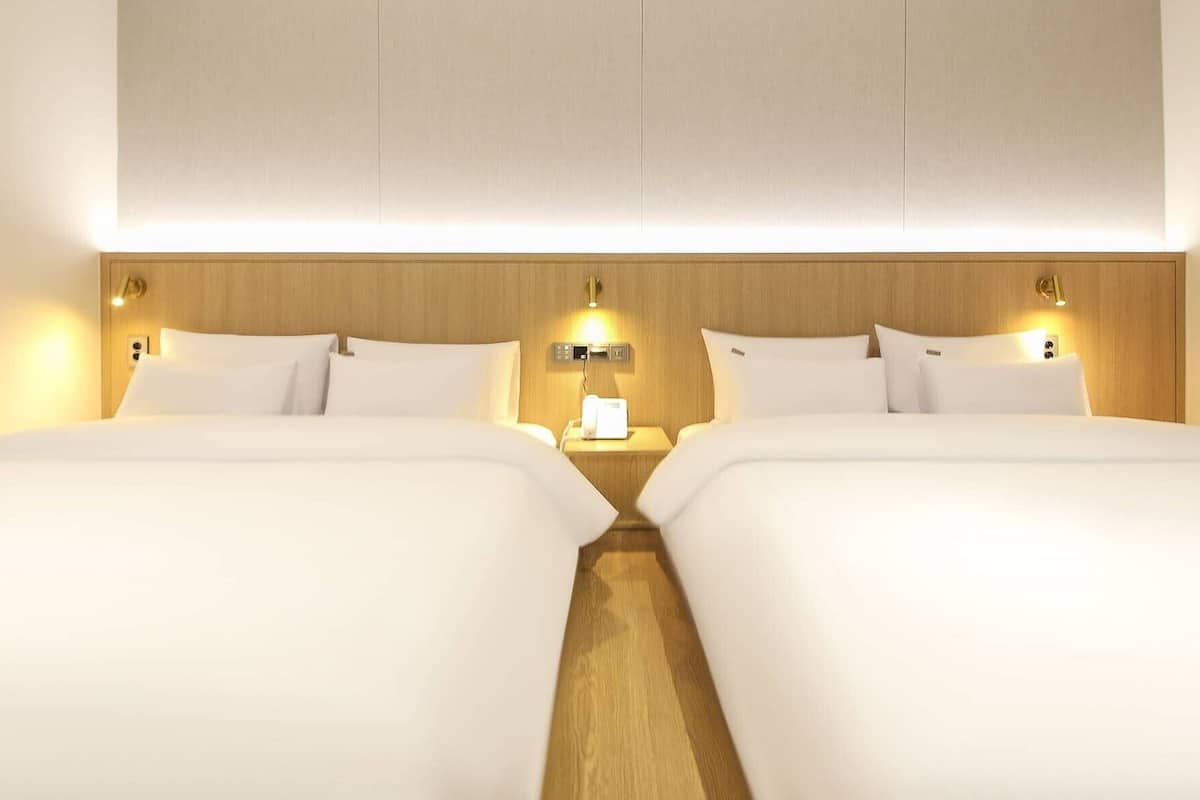 A hotel room with two beds, a wooden headboard, bedside lamps, and a nightstand with a phone and a lamp.