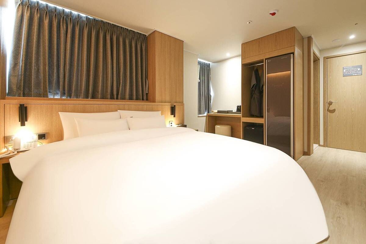 A hotel room with a large bed, a wardrobe, a desk, and a bathroom.