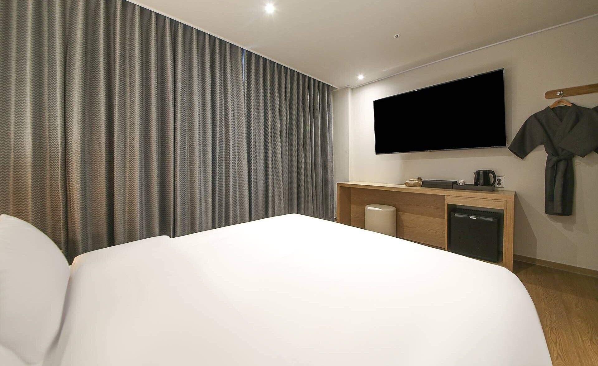 Habitación de hotel con una cama grande, un escritorio con televisor de pantalla plana, una cafetera y una bata colgada en un perchero.