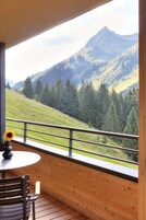 Un balcón con suelo de madera, una mesa redonda con un jarrón de girasoles y vistas a un paisaje montañoso.