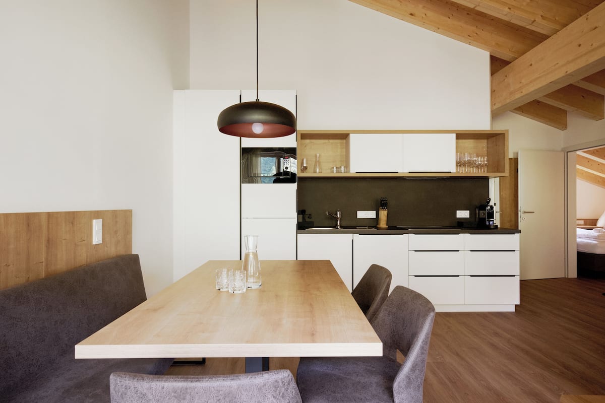Une cuisine moderne avec des meubles blancs, une table à manger en bois et un luminaire suspendu.