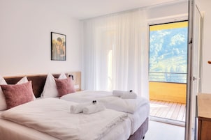 Habitación de hotel con dos camas, ropa de cama blanca, un cuadro en la pared y un balcón con piso de madera.