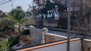 Un balcón con vista a una calle, un muro de piedra y un árbol.