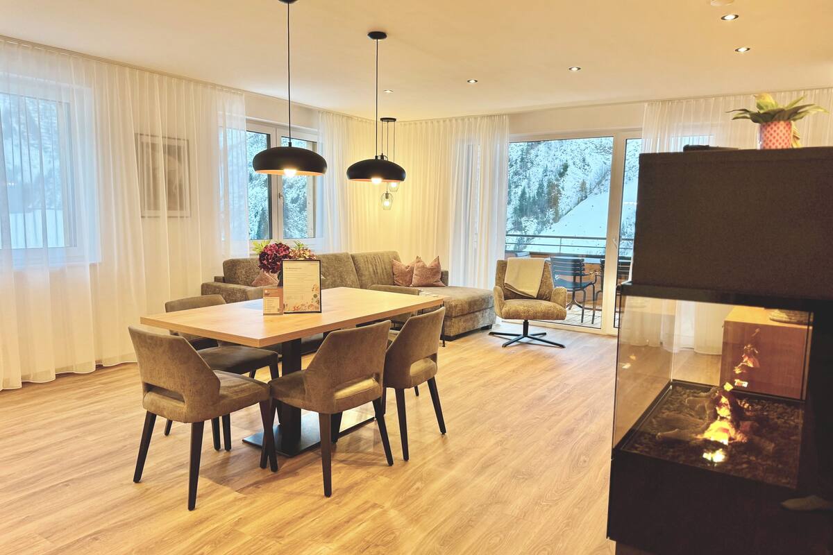 A modern living room with a wooden dining table, comfortable seating, and a large TV.
