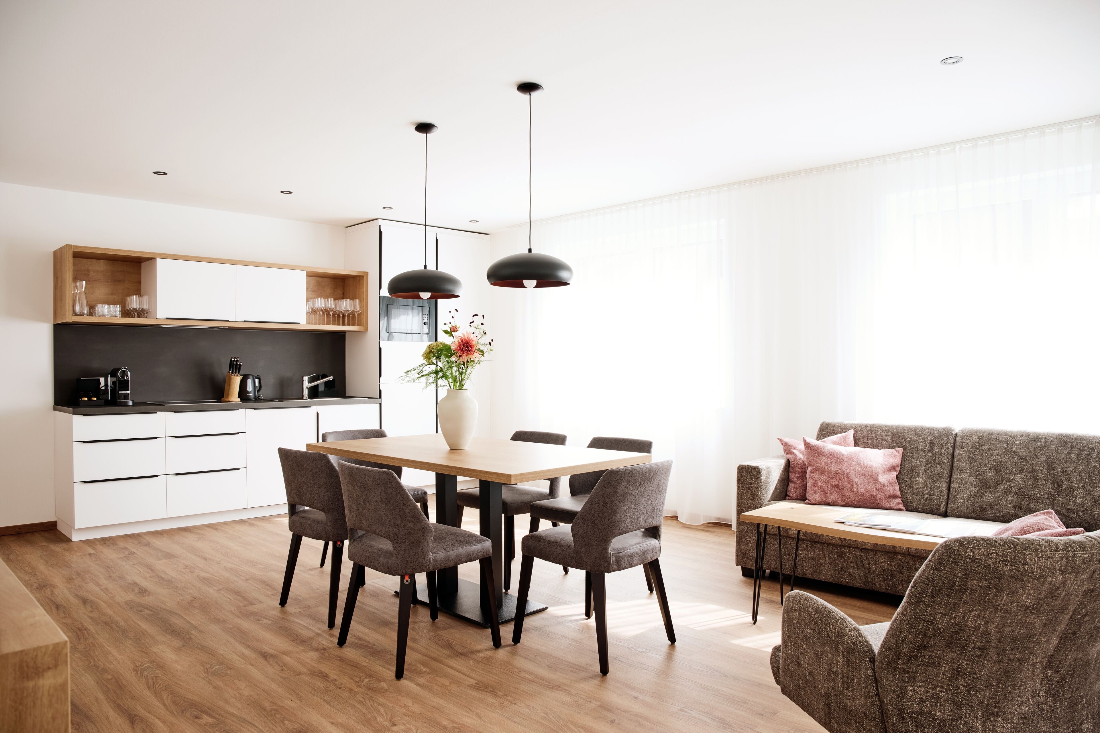 A modern kitchen with white cabinets, a dining table with chairs, and pendant lights.