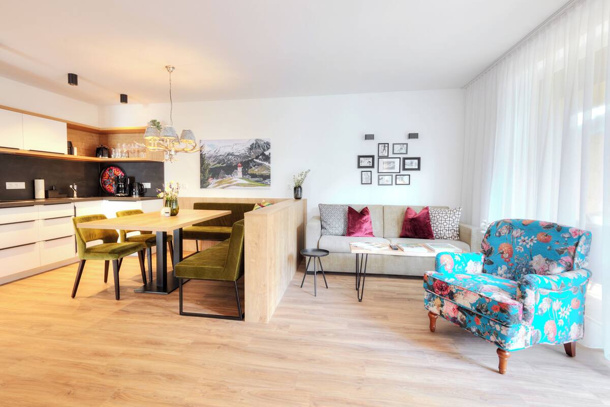 A modern kitchen with a dining area, a sofa, and a floral armchair.