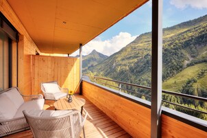 Un balcón de madera con mobiliario de mimbre y una mesa, con vistas a un paisaje montañoso.