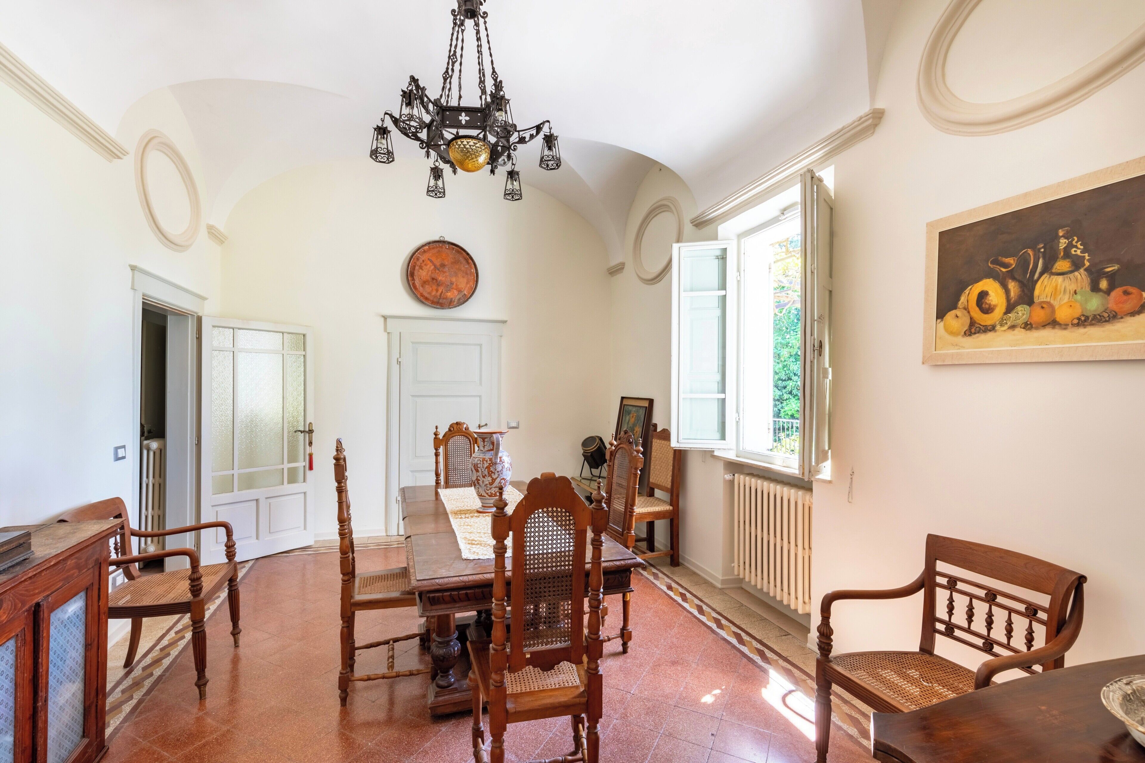 A dining room with a wooden table, chairs, a chandelier, and a painting on the wall.