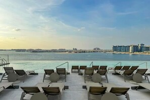 A rooftop pool area with lounge chairs and a view of the city skyline across the water.