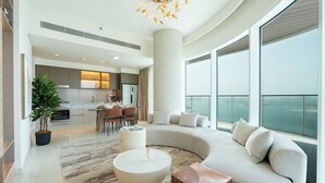 A modern living room with a curved sofa, a round coffee table, and a large window offering a view of the city. - KeyRock - Palm & Sea View with Pool (Dubai)