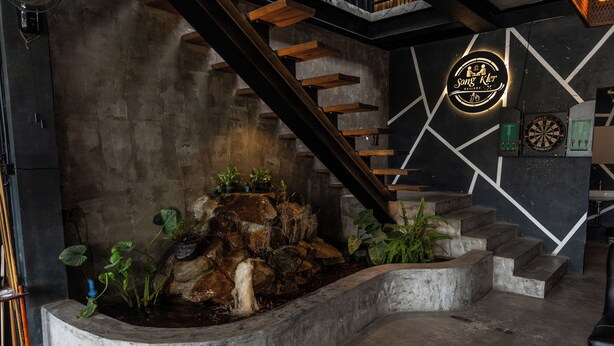A modern interior with a concrete staircase, a small indoor waterfall, and a dartboard on the wall. - SongKler (Ko Pha-ngan)