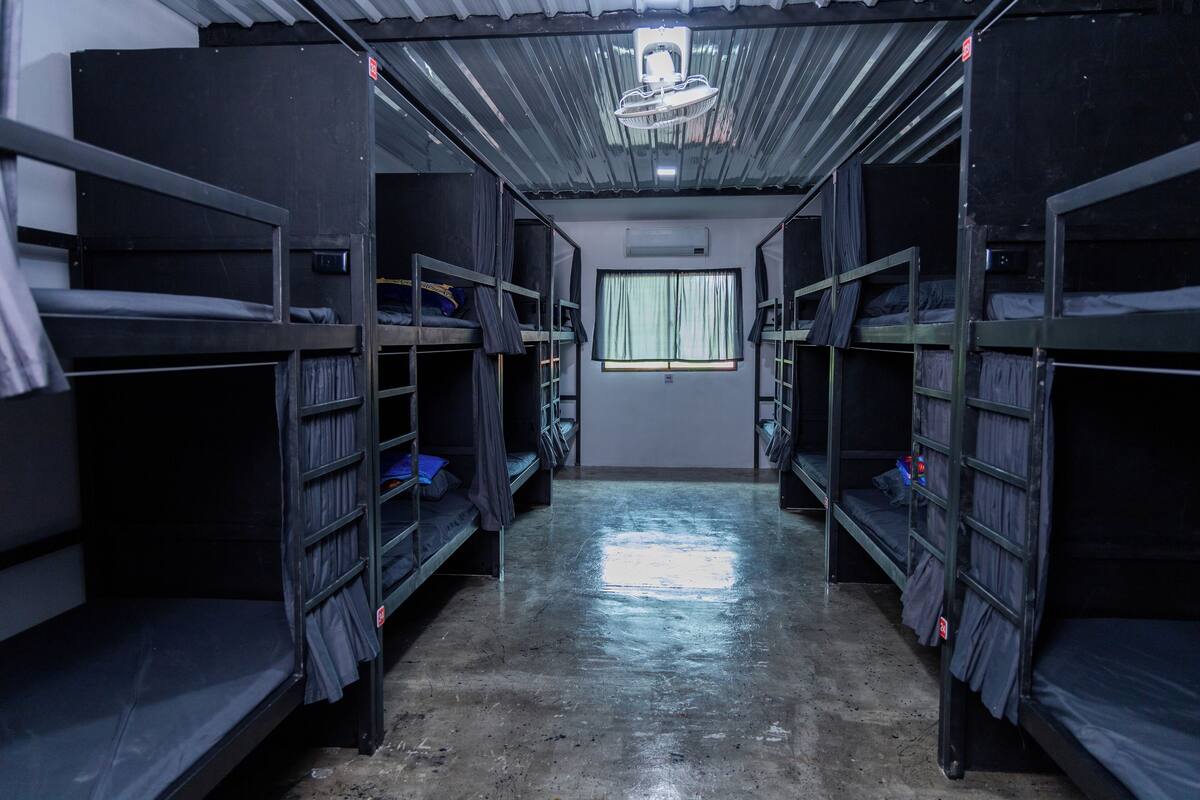 A dormitory room with bunk beds, a window with curtains, and a ceiling fan.