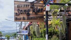 A restaurant named 'Song Kler' with a signboard, parked motorcycles, and a sidewalk with potted plants. - SongKler (Ko Pha-ngan)