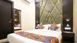 A neatly made bed with a colorful geometric-patterned bedspread, a large mirror, and a wall with a geometric-patterned headboard. - Sky Suites By Glitz Hotels (Mumbai)