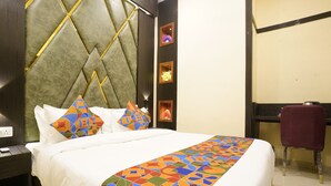 A hotel room with a large bed, a headboard with a geometric pattern, a desk with a chair, and a wall with framed pictures. - Sky Suites By Glitz Hotels (Mumbai)